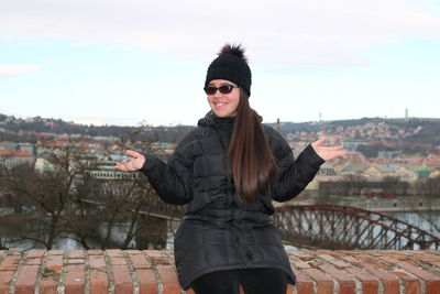 Portrait of young woman standing in city against sky