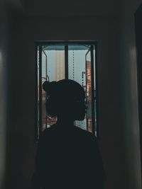 Silhouette woman looking away while standing against window at home