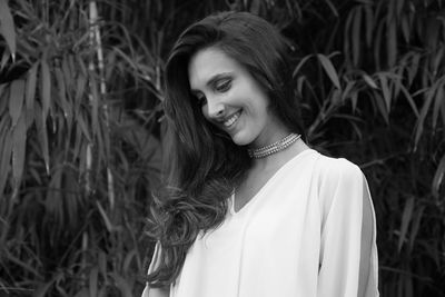 Thoughtful smiling young woman standing against trees