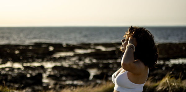 Rear view of woman standing at sea shore against sky