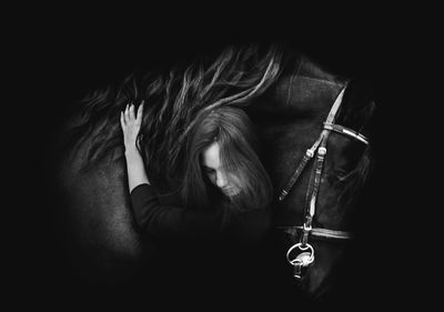 Digital composite image of woman embracing horse against black background