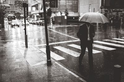 Man with umbrella walking on city street during monsoon