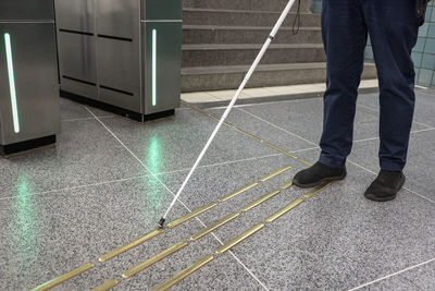 Low section of person with white cane standing at metro station