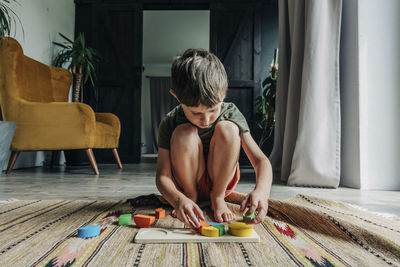 Boy playing with toy blocks crouching on carpet at home