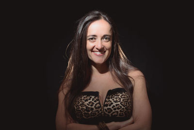 Portrait of woman smiling while standing against black background