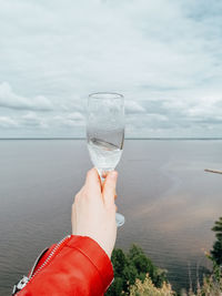 Hand holding glass of water against sky