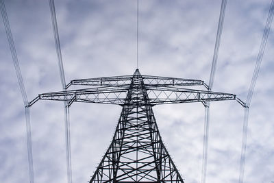 Low angle view of electricity pylon against cloudy sky