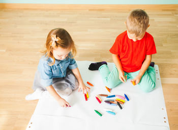High angle view of siblings sitting on wooden floor