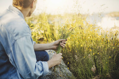 Side view of young man holding at flowers by plants