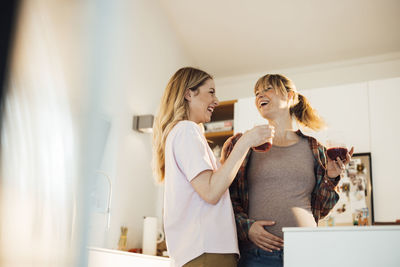 Happy pregnant woman enjoying drink with sister at home