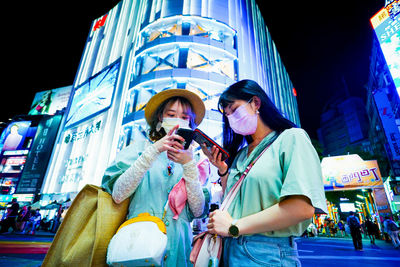 Young female friends using mobile phone in city at night