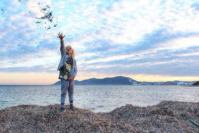 Full length of girl throwing leaves while standing on beach against sky