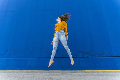 Young woman jumping in front of a blue wall