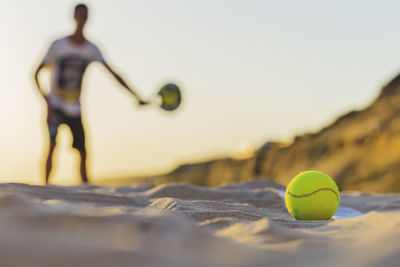 Close-up of yellow tennis ball on sand at beach against sky during sunset