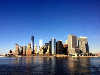 Financial district by river against clear blue sky