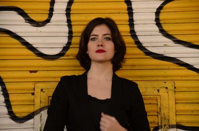 Portrait of beautiful young woman standing against yellow wall