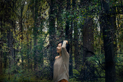 Woman standing by tree trunk in forest