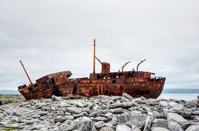 Abandoned ship on rock in sea against sky