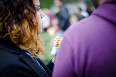 Woman eating fast food while standing by man in city