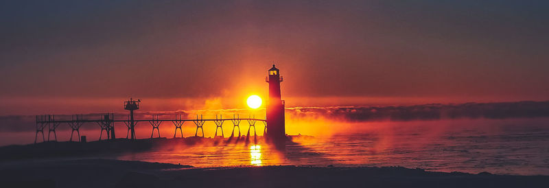 Lighthouse by sea against sky during sunset