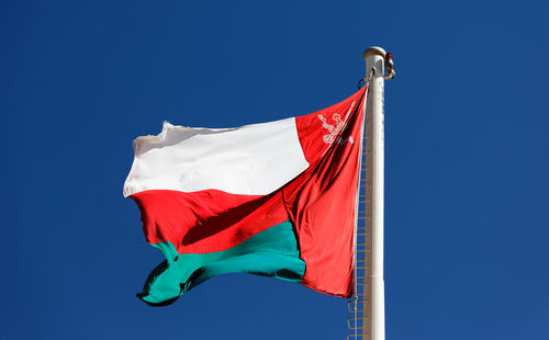 Low angle view of omani flag waving against clear blue sky