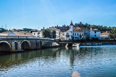 Arch bridge over river by buildings against sky