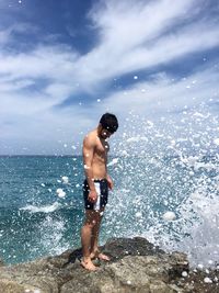 Full length of shirtless man standing in sea against sky