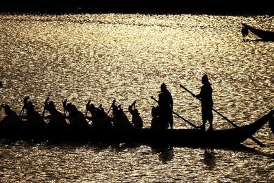 Silhouette people by boats in sea against sky