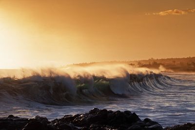 Waves splashing on shore against sky during sunset