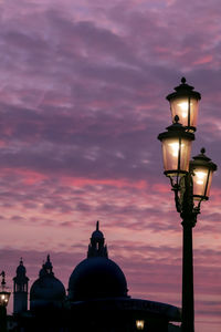 Low angle view of illuminated street light by building against sky