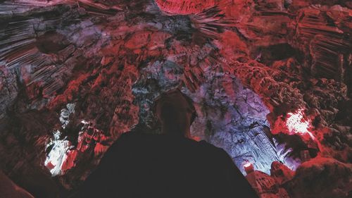 Low angle view of man standing at illuminated red cave