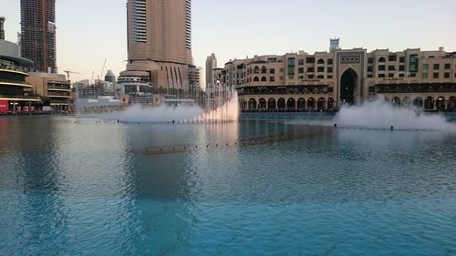 Fountain spraying at lake against sky in city