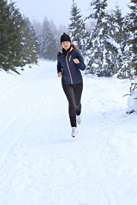 Woman running on snow covered field against sky