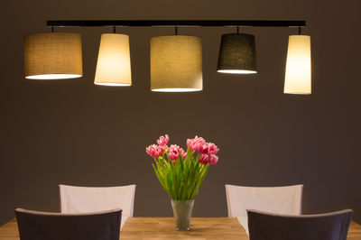 Flower vase on table against illuminated wall at home