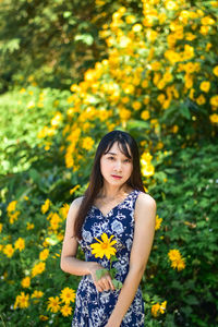 Portrait of beautiful woman standing against yellow flowering plants