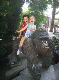 Portrait of smiling woman with arms raised against trees