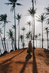 Rear view of young woman standing at beach against sky during sunny day