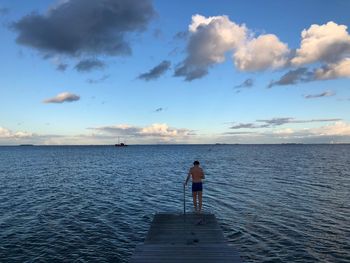 Rear view of man standing on jetty by sea against sky