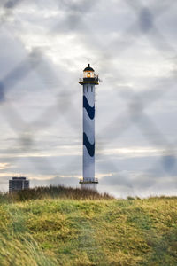 Lighthouse on field against sky
