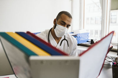 Male healthcare worker reading files at medical clinic during covid-19