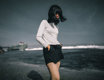 Young woman standing on beach against sky