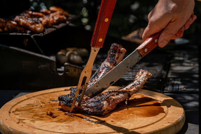 Hand cutting meat with knife and fork. grilled ribs on the barbecue in summer.