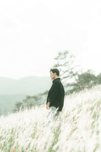 Side view of young man standing on field against sky
