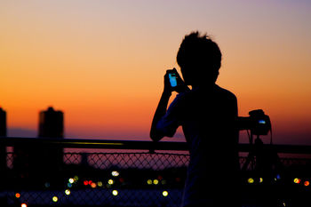 Silhouette man using phone against orange sky