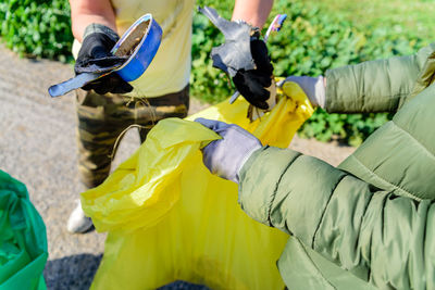 Midsection of people collecting garbage while holding yellow plastic garbage bag