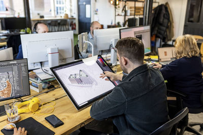 Architect working on graphics tablet with colleagues at desk in office