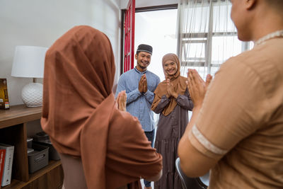 Rear view of couple greeting guest at home