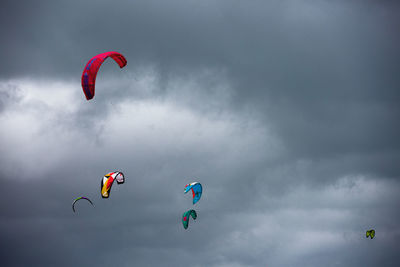 Low angle view of people paragliding against sky