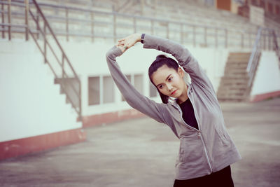 Young woman stretching while standing against built structure