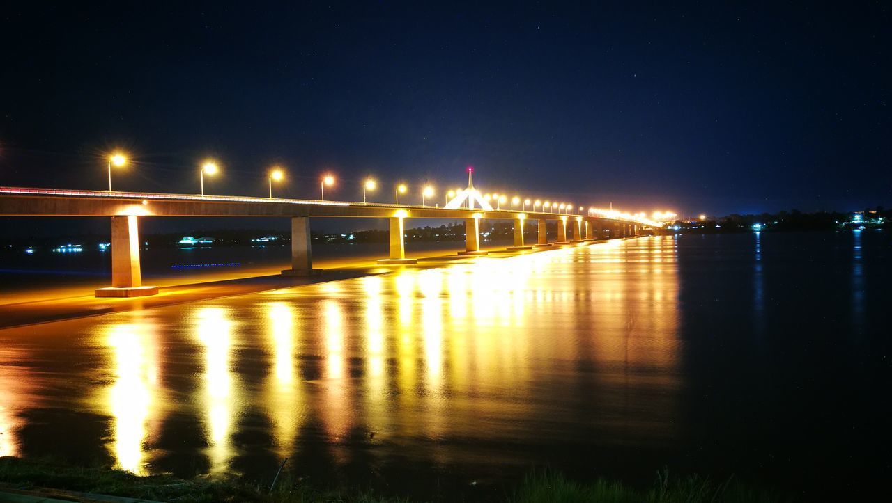 ILLUMINATED BRIDGE OVER RIVER AGAINST SKY